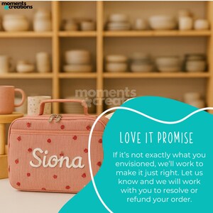 May include: A pink corduroy travel bag with a handle, zipper, and the name "Siona" embroidered in white. The bag is decorated with small red strawberry patterns. The background features shelves with various ceramic items.
