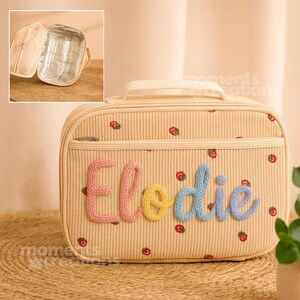 May include: Cream-colored corduroy cosmetic bag with the name "Elodie" in pink, yellow, and blue yarn. The bag has a handle and is decorated with small red and green floral accents. The interior is visible in a smaller inset image.