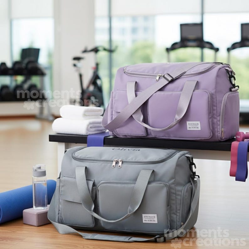 May include: Two duffel bags, one lavender and one gray, sit on a bench. Both bags have multiple pockets, shoulder straps, and the text "Olivia" on the gray bag. A blue yoga mat, water bottle, and exercise bands are nearby.