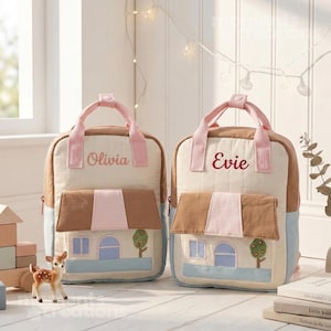 May include: Two beige and brown backpacks with pink accents. Each backpack features a house design with a brown roof, blue walls, and a tree. One backpack says "Olivia" and the other says "Evie".