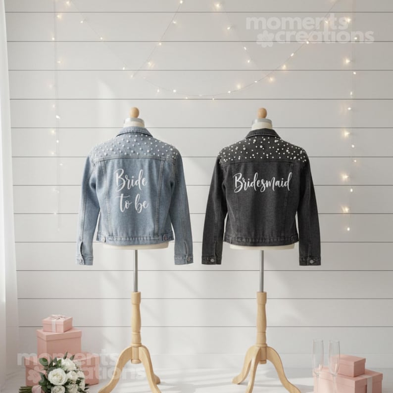 K&ouml;nnte beinhalten: Zwei Jeansjacken auf einer Pr&auml;sentation. Eine ist hellblau mit dem Text "Bride to be" und Perlenverzierungen. Die andere ist dunkelgrau mit dem Text "Bridesmaid" und &auml;hnlichen Verzierungen. Beide stehen auf Holzst&auml;ndern.