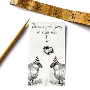 Op de afbeelding: Een novelty kaart met de tekst "There's a party going on right here" en illustraties van schapen met feesthoeden. Een kleine schapenpin staat boven de schapenillustraties. Een vintage meetlint staat op de achtergrond.