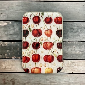 May include: A white glass chopping board with a vintage illustration of red and black cherries. The cherries are arranged in a repeating pattern on the board.