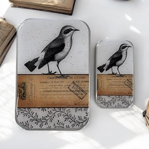 Puede incluir: Dos latas de metal plateadas con una ilustración en blanco y negro de un pájaro en cada una. La lata más grande tiene el texto "CHOCOLATERIE DE L'UNION" y "CREDIT LYONNAIS". La lata más pequeña tiene el texto "CHOCOLATERIE DE L'UNION".