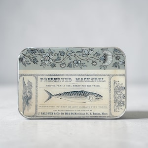 May include: Rectangular tin with a vintage design featuring the text "PRESERVED MACKEREL." The tin has a light blue background with floral and botanical illustrations. A detailed drawing of a mackerel is centered on the label.