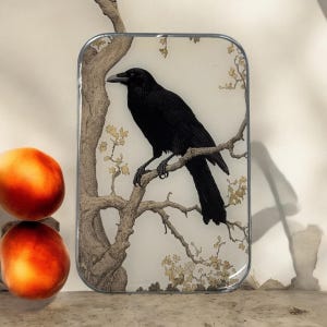 May include: A black crow perched on a branch of a tree with delicate, light brown branches and small, light yellow flowers. The background is a light cream colour.