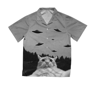 Könnte beinhalten: Ein graues, kurzärmeliges Hemd mit Knöpfen und einem Schwarzweißbild einer Katze, die zu einem Himmel voller fliegender Untertassen schaut.