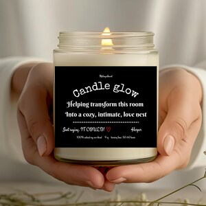 May include: A white candle with a black label that reads "Candle glow" and "Helping transform this room into a cozy, intimate, love nest." The label also includes the text "Just saying, IT COULD!" with a red heart and "Harper".