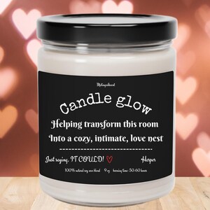 May include: A black and white candle jar with the text "Candle glow" and "Helping transform this room into a cozy, intimate, love nest. Just saying, IT COULD!" with a small heart symbol. The candle is 9 oz and has a burn time of 50-60 hours.