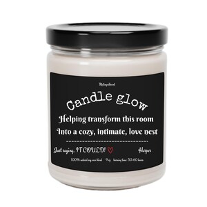 May include: A black and white candle jar with the text "Candle glow" and "Helping transform this room into a cozy, intimate, love nest. Just saying, IT COULD!" with a red heart. The candle is 9 oz and has a burn time of 50-60 hours.