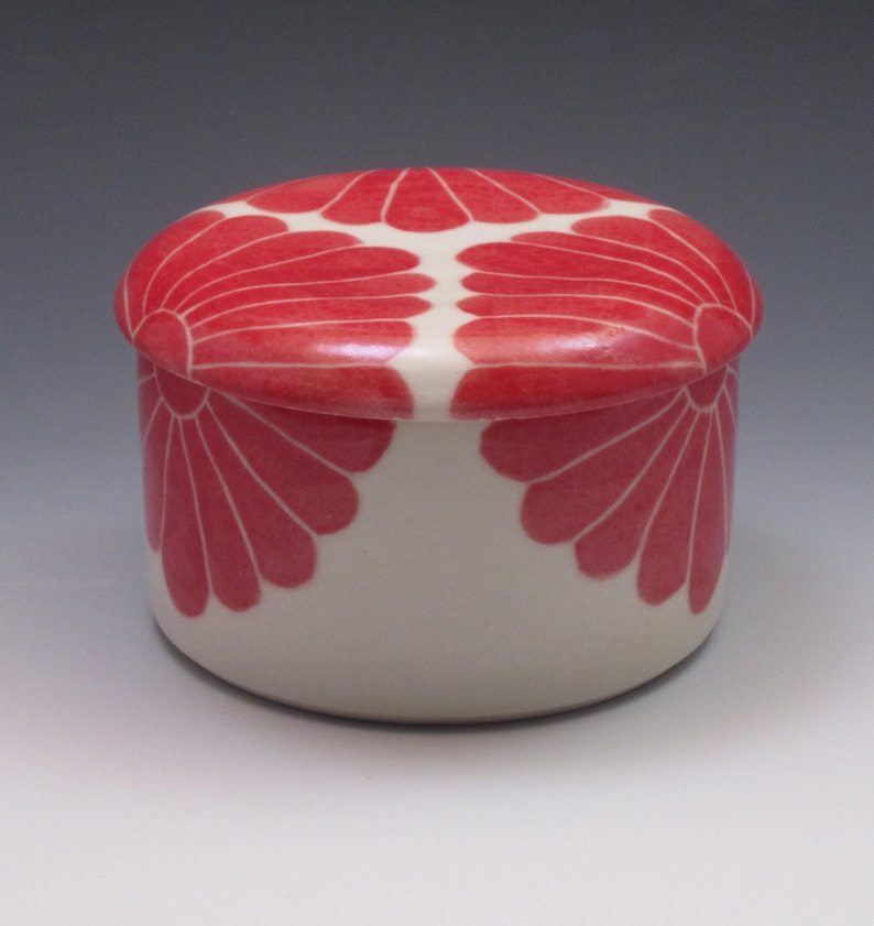 Pu&ograve; includere: Una scatola portaoggetti in ceramica bianca con coperchio. La scatola e il coperchio sono decorati con un motivo floreale rosa.
