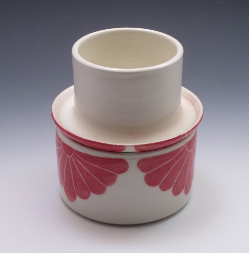 Pu&ograve; includere: Un porta burro in ceramica bianca con un design floreale rosa. Il porta burro ha un coperchio rimovibile e una base con un motivo floreale rosa.