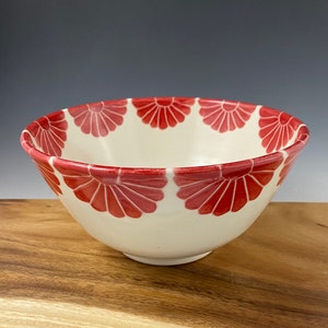 May include: A white ceramic bowl with a red floral pattern around the rim. The bowl is sitting on a wooden surface.