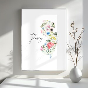 May include: A white print with the outline of the state of New Jersey filled with watercolor flowers. The text "new jersey" is written in cursive below the state outline.