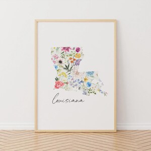 May include: A framed print featuring the outline of Louisiana filled with a floral pattern. The flowers are in various colors, including pink, purple, yellow, and blue. The word "Louisiana" is written in cursive below the state outline.