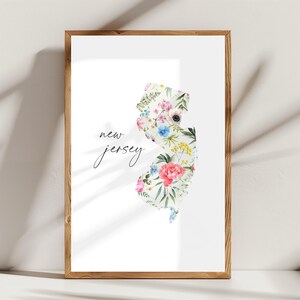May include: A white print with the text "new jersey" in black script. The state of New Jersey is outlined in white and filled with a watercolor floral design in shades of pink, blue, yellow, and green.