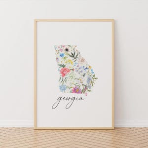 May include: A white print with a floral design in the shape of the state of Georgia. The text "georgia" is written in black cursive below the floral design.