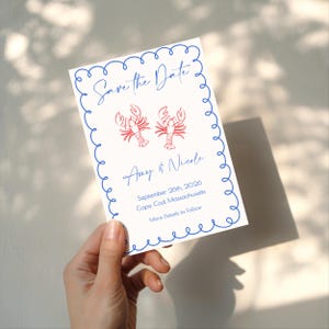 May include: A white invitation card with a blue scalloped border and text that reads "Save the Date." Two red lobster illustrations are above the names "Amy & Nicole." The date and location are also included.