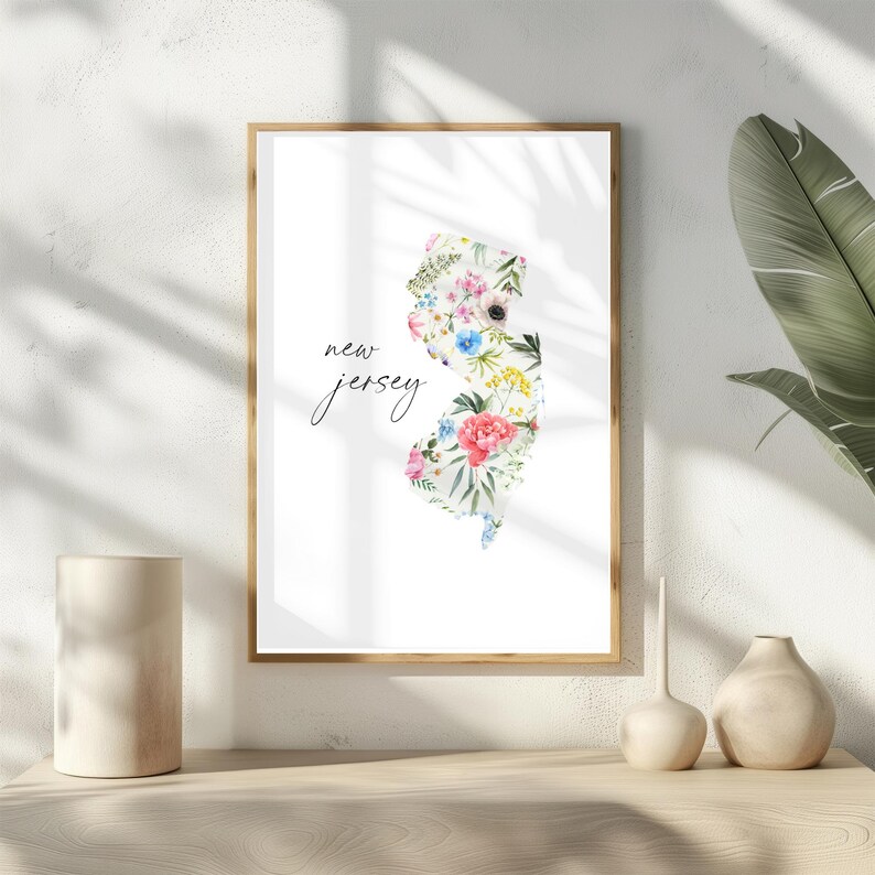 May include: A white framed print with a floral design of the state of New Jersey. The text "new jersey" is written in black cursive script.