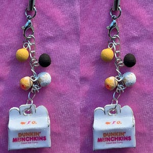 May include: A charm featuring a miniature white box with the words "DUNKIN' MUNCHKINS" in red. The charm is attached to a chain with various colorful bead-like charms and an orange lanyard.