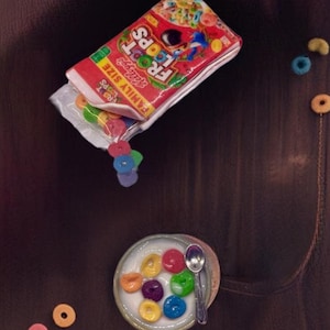 May include: A bowl of cereal with milk and colorful cereal pieces. The cereal box is in the background and says "Froot Loops Family Size".