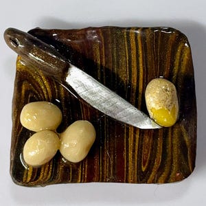 May include: A miniature wooden cutting board with a silver knife, three white ceramic potatoes, and one yellow ceramic potato.
