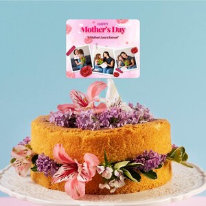 Könnte beinhalten: Ein gelber Kuchen, der mit lila und rosa Blumen verziert ist. Auf dem Kuchen liegt eine Karte mit dem Text "Happy Mother's Day" und einem Foto-Collage von drei Frauen.