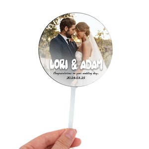 May include: A round, white, wedding cake topper with a photo of a couple and the text "LORI & ADAM Congratulations on your wedding day... 2024.03.25"