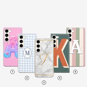 May include: Five smartphone cases featuring distinct designs: a pink case with a puffy letter A, a light blue gingham case with a letter M, a white marble case with a gold letter J, a dark green case with a large letter K, and a striped case with a letter A.