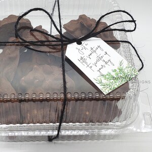 May include: A clear plastic container filled with chocolate treats tied with black twine and a gift tag that reads "Just a little something to sweeten up your day".