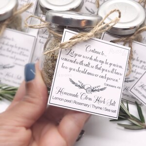 May include: Small glass jar filled with homemade citrus herb salt, tied with twine and a tag. The tag reads "Homemade Citrus Herb Salt" with ingredients listed. The jar has a silver lid and is surrounded by other jars.