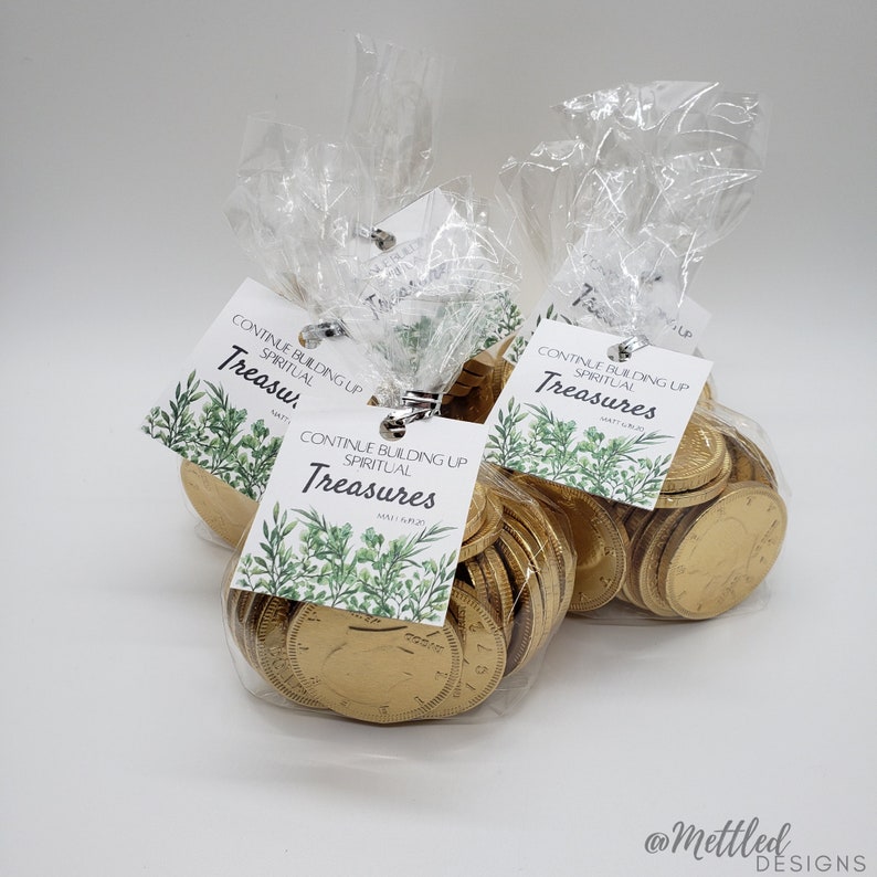 May include: Three clear plastic bags filled with gold chocolate coins. Each bag has a white tag with green foliage and the text "Continue Building Up Spiritual Treasures" with a scripture reference.