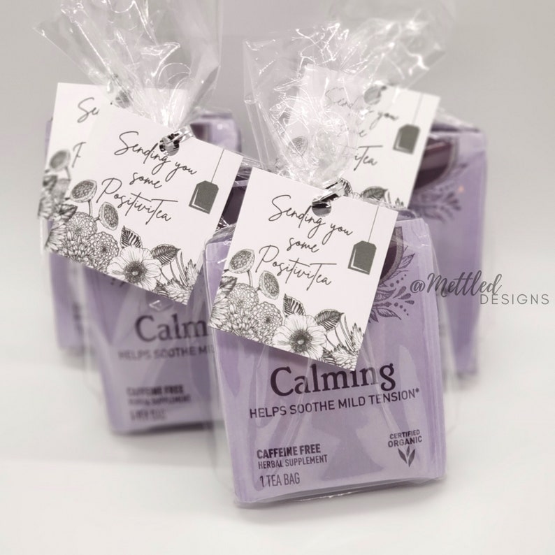 May include: Several lavender tea bags are packaged in clear cellophane, each with a tag that reads "Sending you some PositiviTea." The tags feature floral illustrations and a tea bag graphic. The tea bags are labeled "Calming."