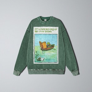 May include: Green sweatshirt with a graphic of a frog in a boat reading a book. The text "IT'S A WHOLE GREAT BIG FUN THING" is above the graphic. The sweatshirt has a crew neck and long sleeves.