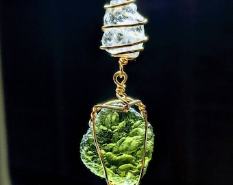 Può includere: Una pietra di peridoto verde avvolta in filo d'oro, appesa a un cristallo di quarzo trasparente avvolto in filo d'oro.