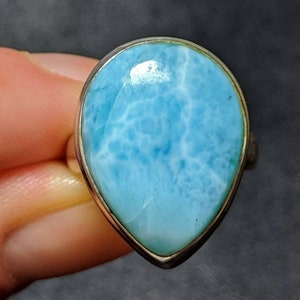 Puede incluir: Un anillo en forma de lágrima con una piedra preciosa azul claro engastada en una banda de plata.