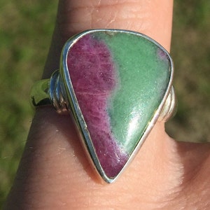 May include: A silver ring with a green and pink gemstone. The gemstone is a triangular shape and has a smooth, polished surface.