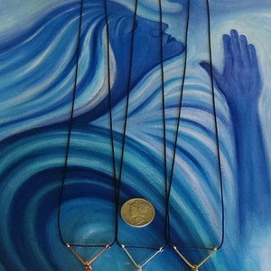May include: Three necklaces with different colored pendants on black cords. The pendants are a rose gold, silver, and gold color. The necklaces are displayed on a blue and white background.