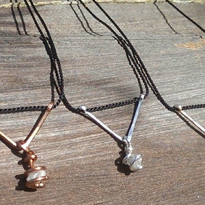 May include: Three necklaces with raw diamond pendants on black cords. The pendants are attached to a V-shaped wire, with the top of the V being a different metal color: copper, silver, and gold.