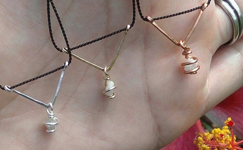 May include: Three necklaces with raw diamond pendants wrapped in wire. The necklaces are on a black cord and have a V-shaped design.