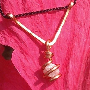 May include: A gold pendant necklace with a raw diamond encased in a spiral of gold wire. The necklace is on a black cord.