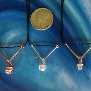May include: Three necklaces with a V-shaped wire pendant and a small crystal wrapped in wire. The necklaces are on a black cord and are displayed on a blue background.