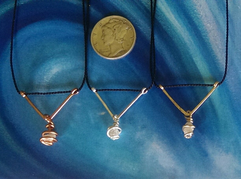 May include: Three necklaces with a V-shaped wire pendant and a small crystal wrapped in wire. The necklaces are on a black cord and are displayed on a blue background.