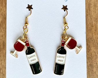 May include: A pair of gold earrings with a red wine glass and bottle charm. The bottle is labeled "Lafite 1982". The earrings are handmade with love in Georgia.