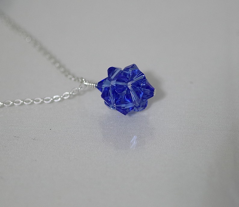 Puede incluir: Un collar de cadena de plata con un colgante de cristal azul en forma de estrella.