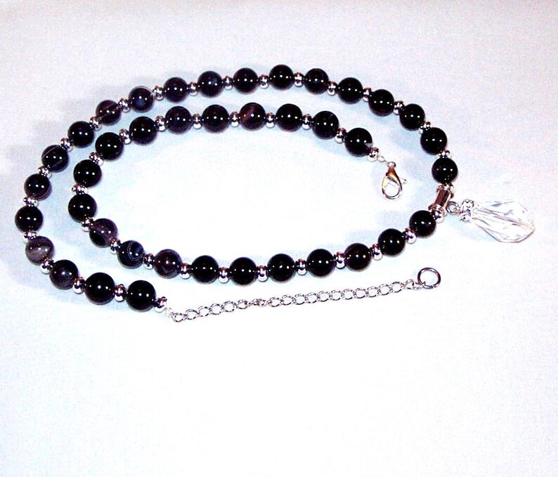 May include: A black beaded necklace with a silver chain and a clear crystal pendant.