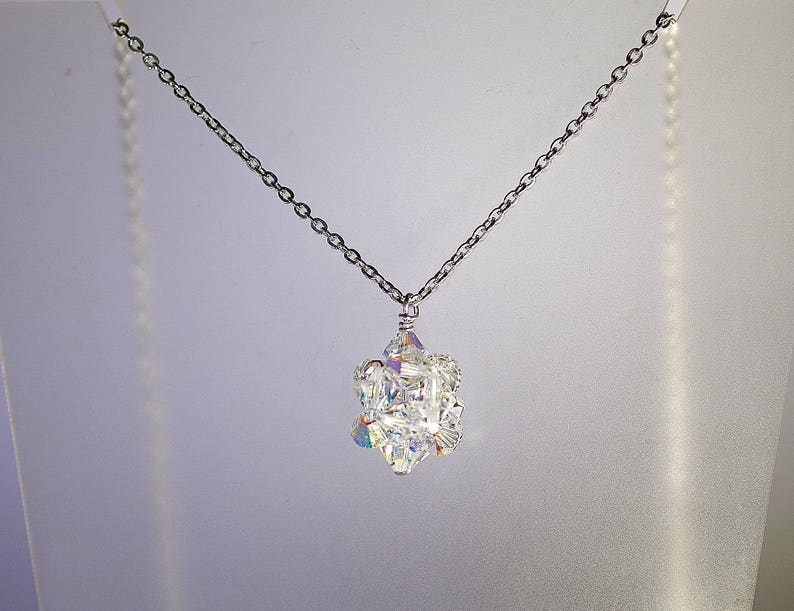 May include: A silver chain necklace with a crystal pendant. The pendant is made of many small, faceted crystals that are arranged in a cluster. The crystals are clear and sparkle in the light.