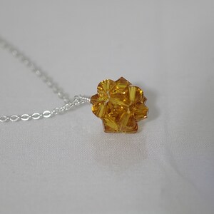 Puede incluir: Un collar de cadena de plata con un colgante de cristal amarillo dorado. El colgante es una esfera hecha de muchas peque&ntilde;as facetas.