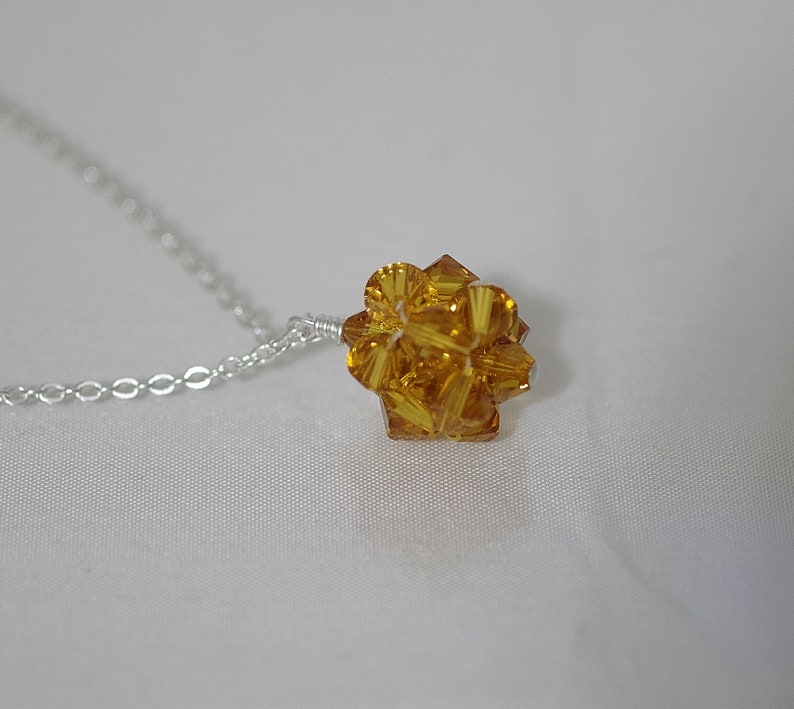 Puede incluir: Un collar de cadena de plata con un colgante de cristal amarillo dorado. El colgante es una esfera hecha de muchas peque&ntilde;as facetas.