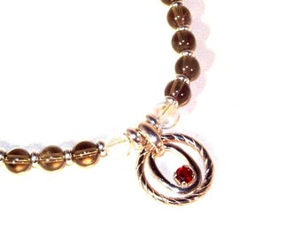 May include: A silver bracelet with brown beads and a silver charm with a red gemstone in the center.